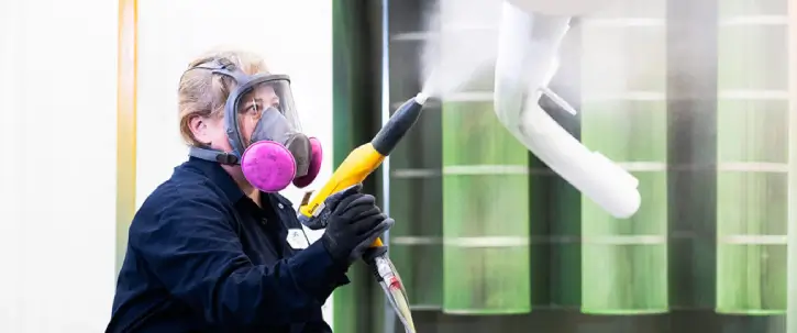 Technicien appliquant un revêtement en poudre sur des pièces métalliques suspendues